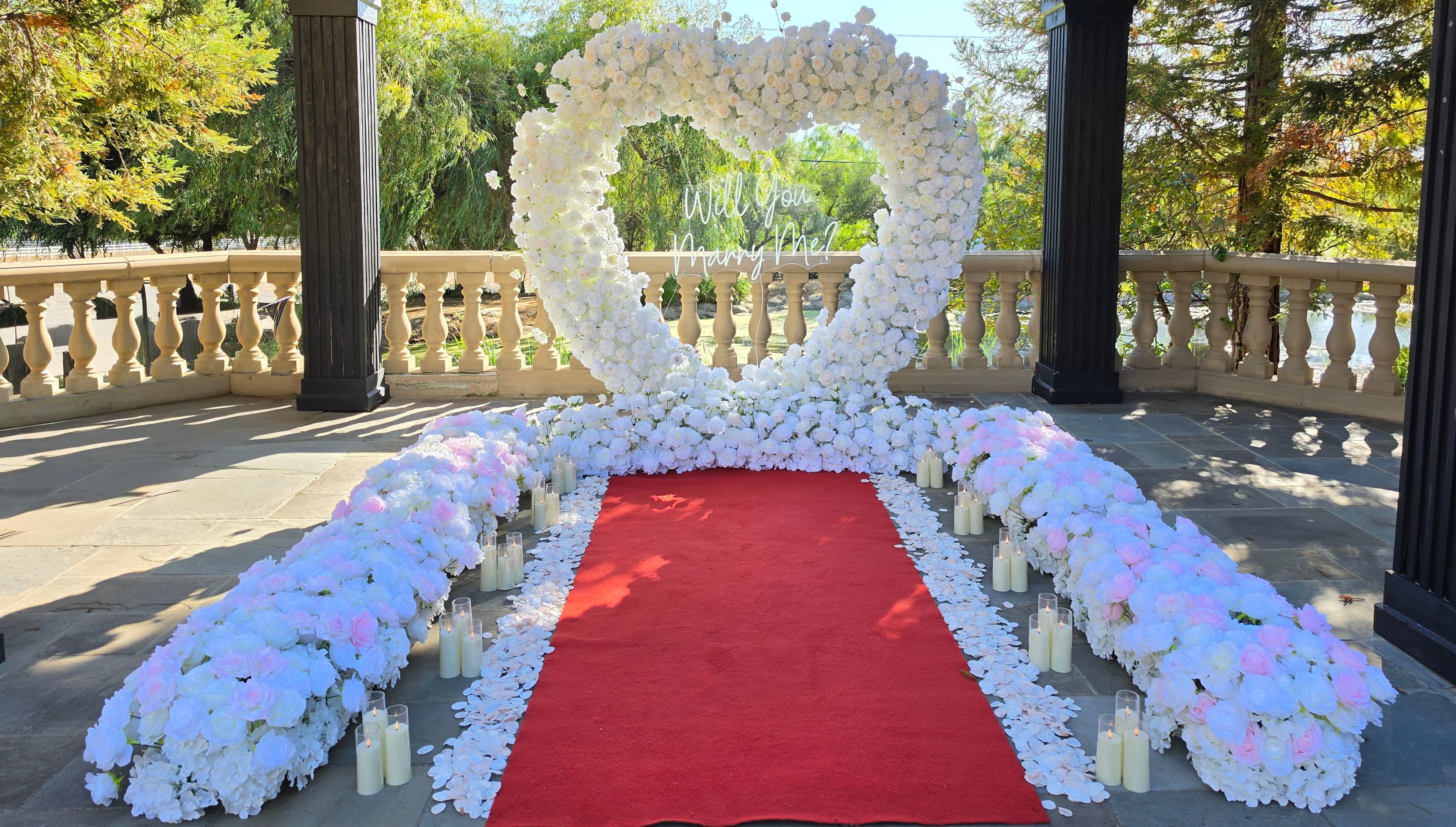 The Masterpiece Package white and pink rose heart arch with "Will You Marry Me?" neon sign, red carpet aisle, and candles under the pavilion at Castillo's Hillside Shire Winery